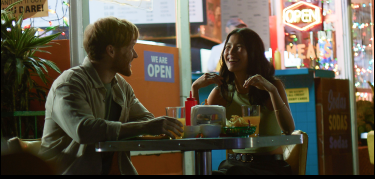 A man and a woman smiling at each other while eating outdoors at a restaurant