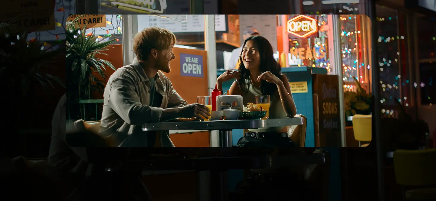 A man and a woman smiling at each other while eating outdoors at a restaurant