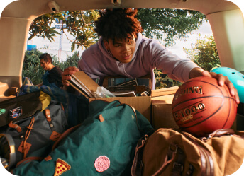 A young man reaching into the trunk of a car to grab a basketball
