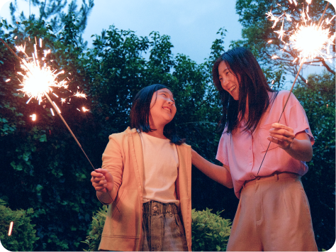 A mom and daughter holding sparklers outdoors