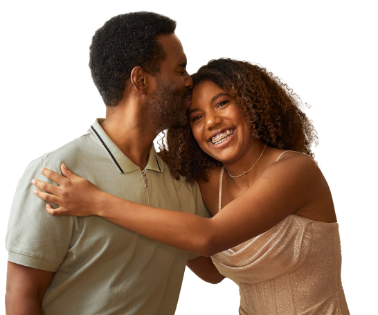 A father kissing his daughter on the forehead as she wraps her arms around him and smiles