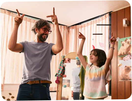 A father and daughter smiling at each other while holding their hands up in the air